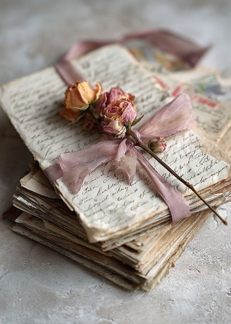 Handwritten letters tied with pink ribbon beside dried roses